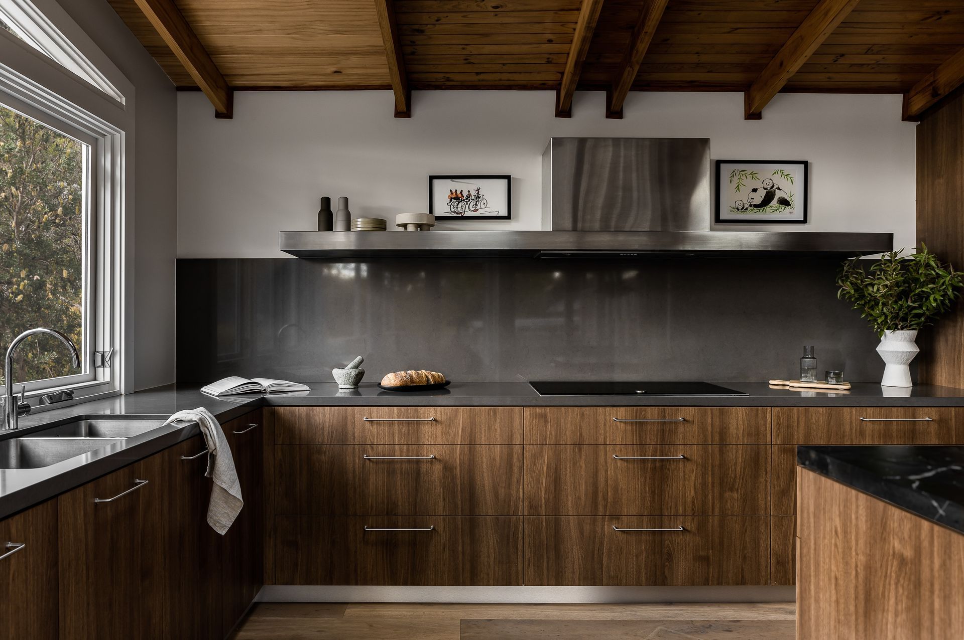 Modern kitchen with wooden cabinets, dark countertops, stainless steel range hood, and window. — Goode By Design in Unanderra, NSW