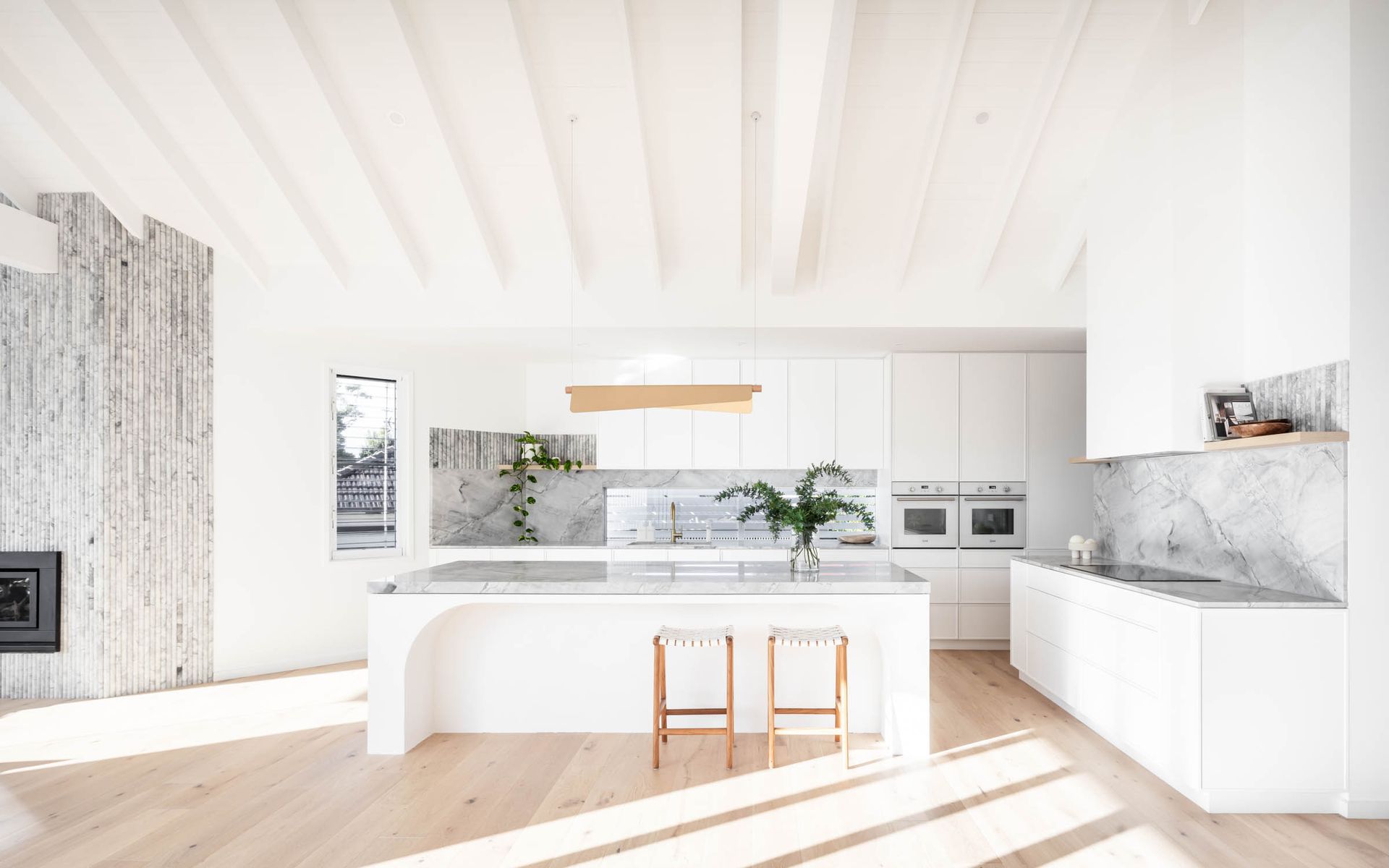 A Kitchen with White Cabinets, Stools and A Large Island — Goode By Design in Unanderra, NSW