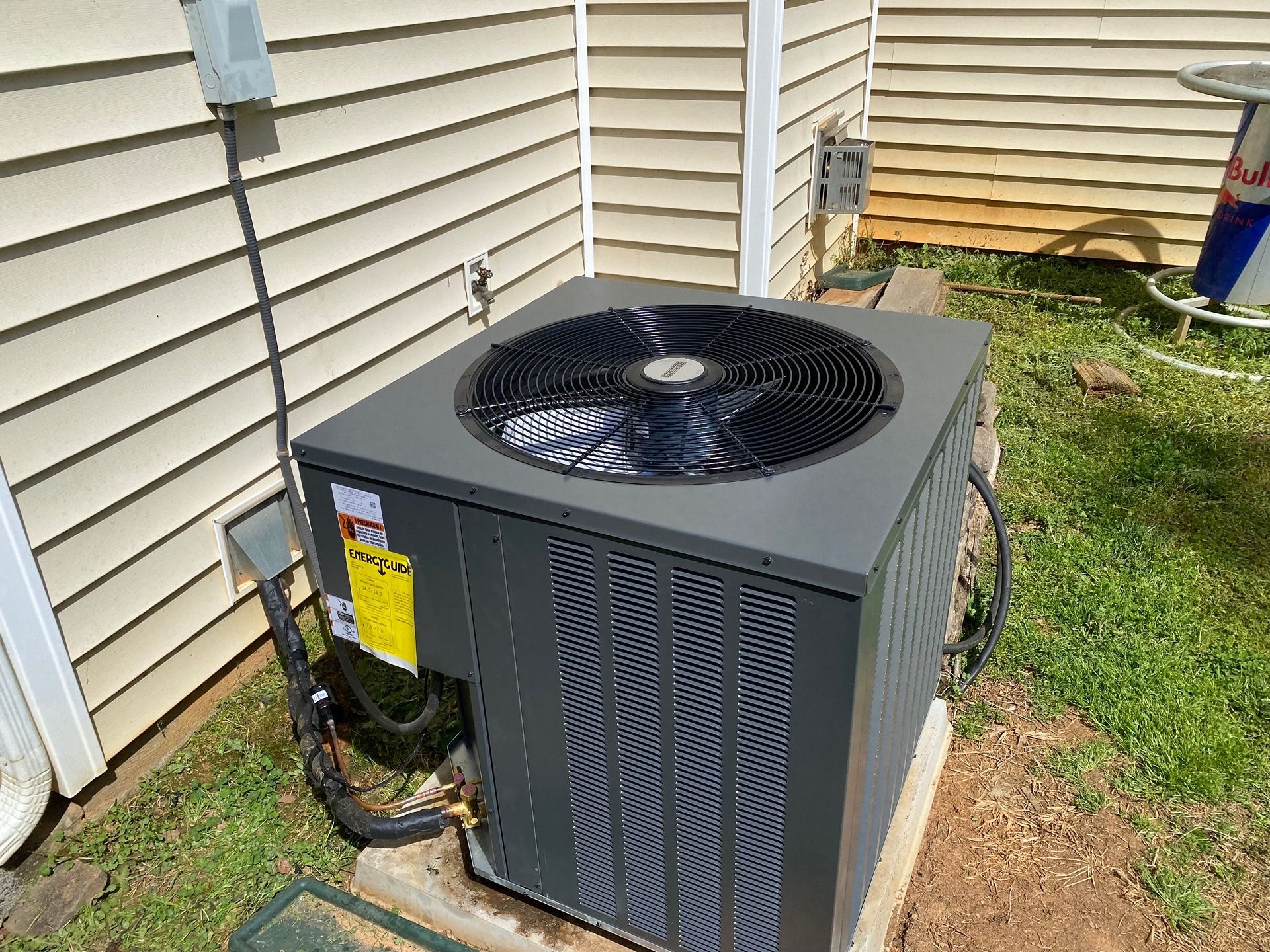 Two outdoor air conditioning units next to a white brick wall, with landscaping nearby.