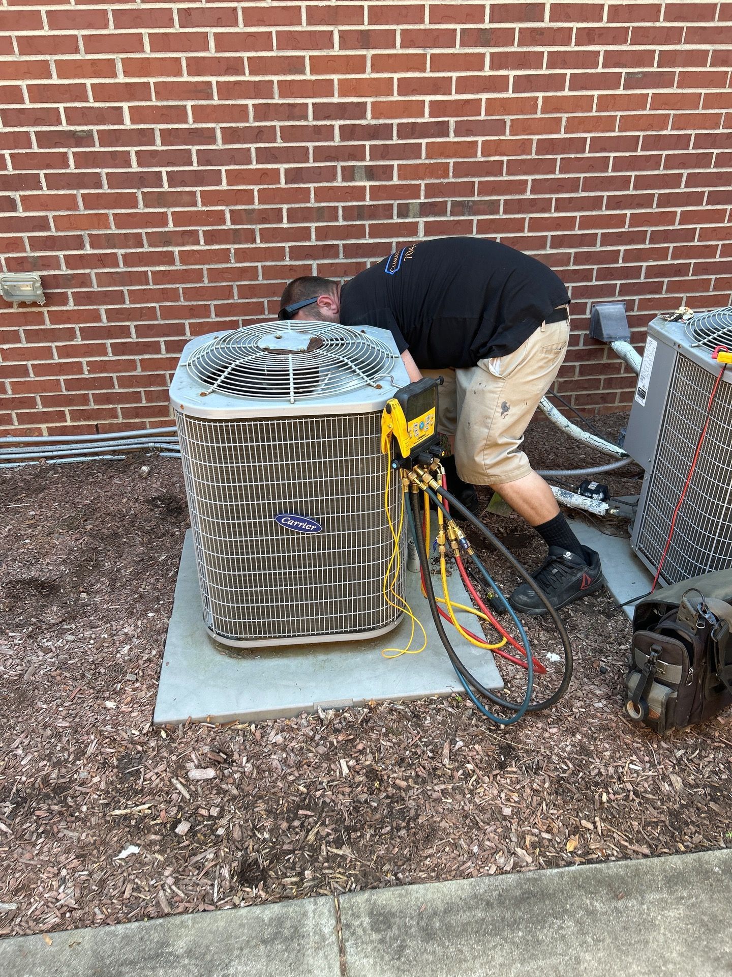 Two workers in safety vests and hard hats inspecting rooftop air conditioning units.