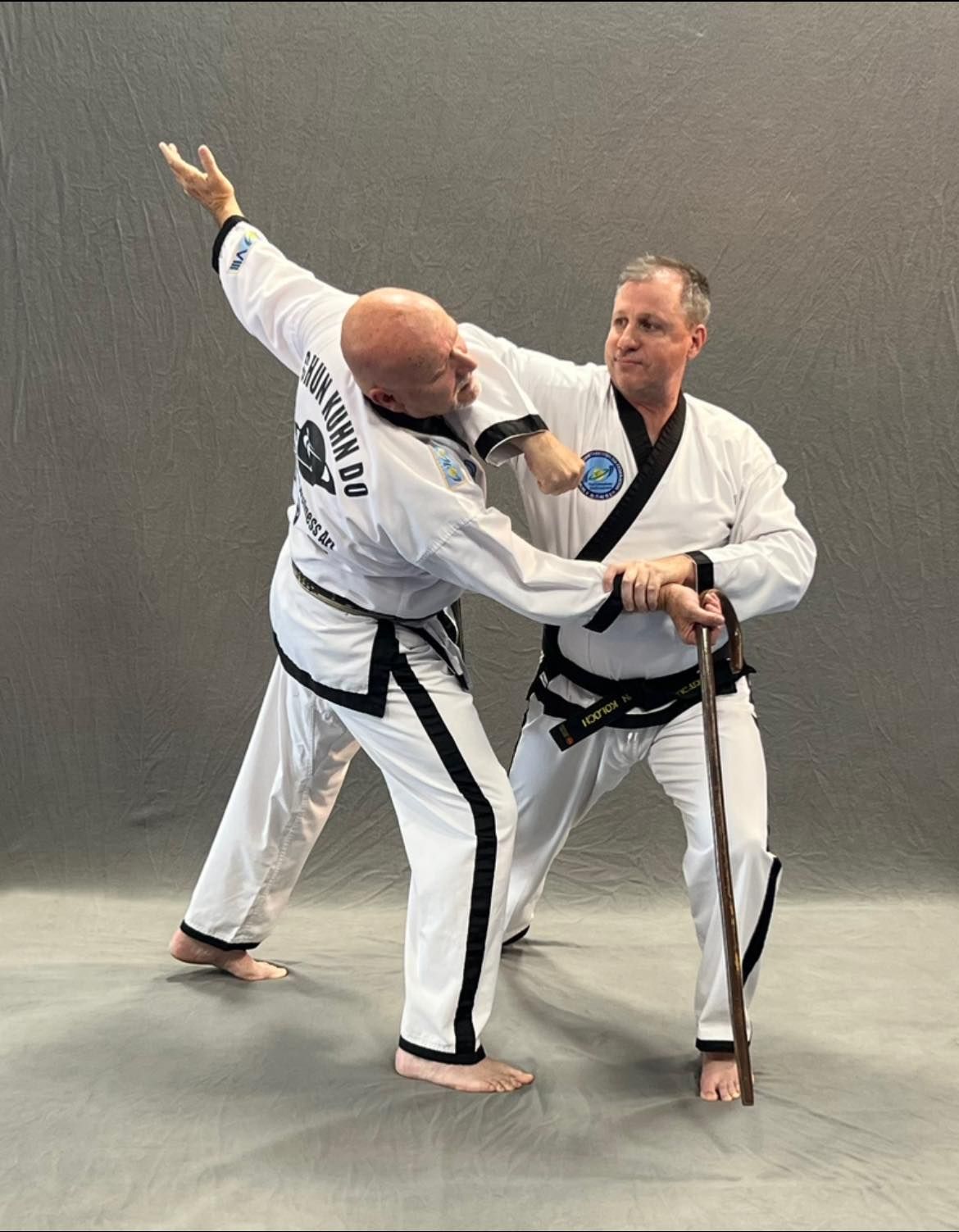 Two men in martial arts uniforms are fighting with a cane