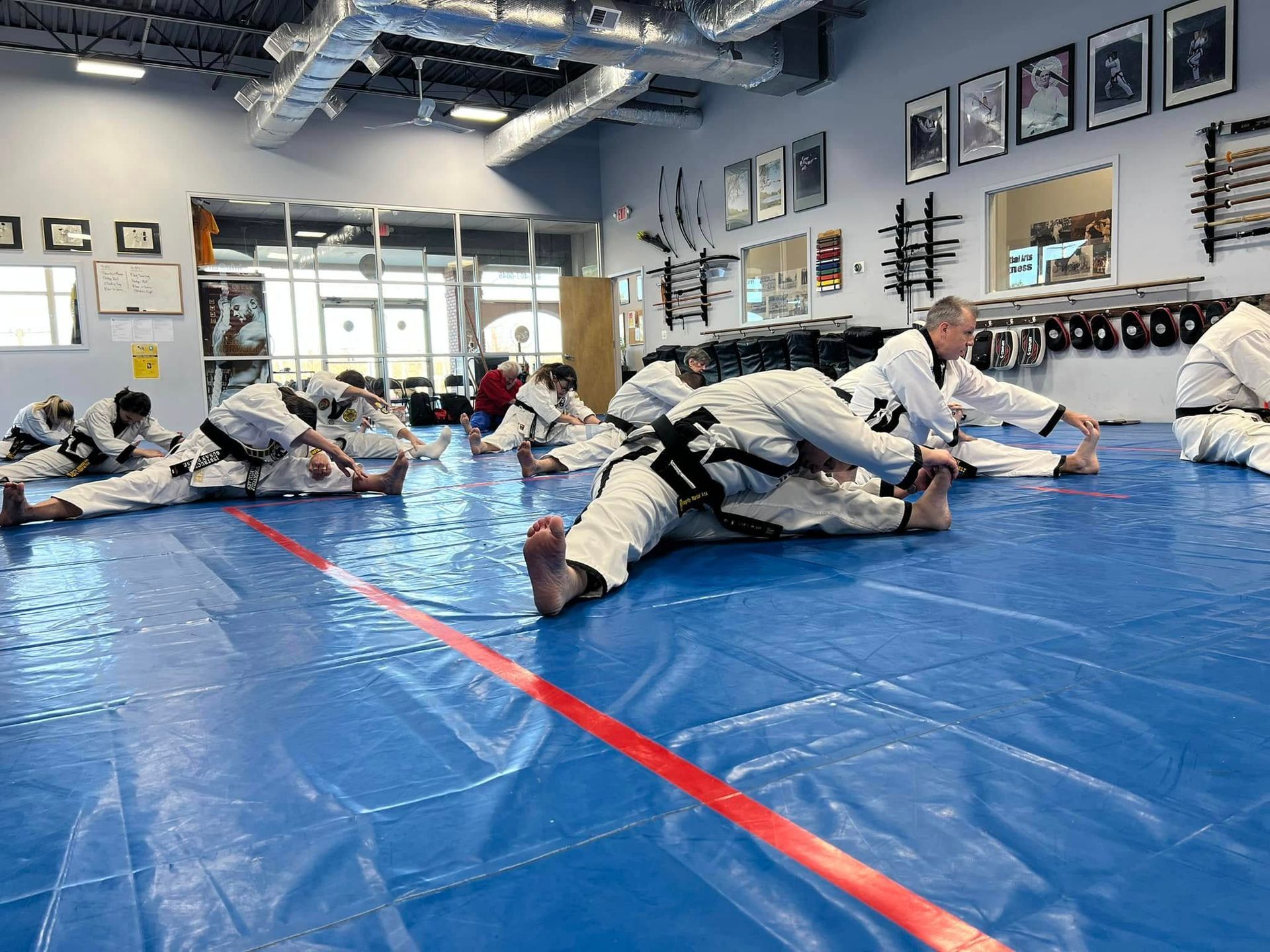 A group of people are stretching on a blue mat in a gym.