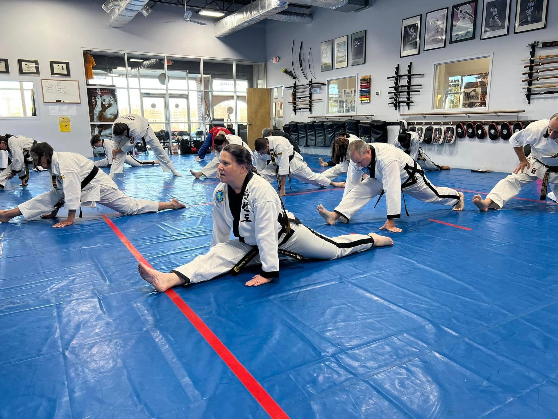 A group of people are stretching on a blue mat in a gym.