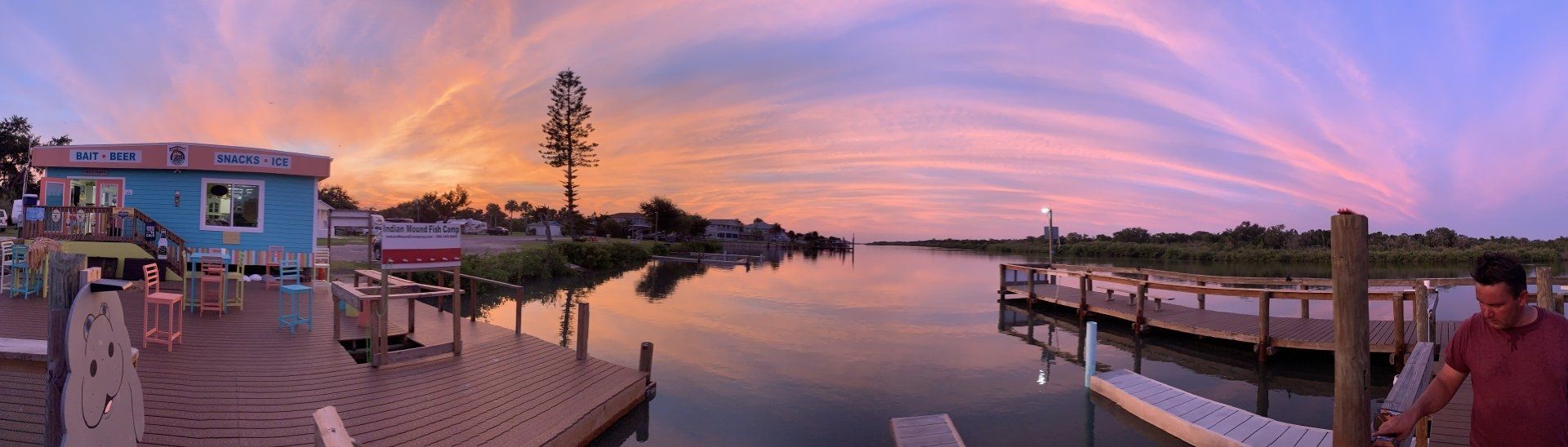 A man is standing on a dock overlooking a river at sunset.