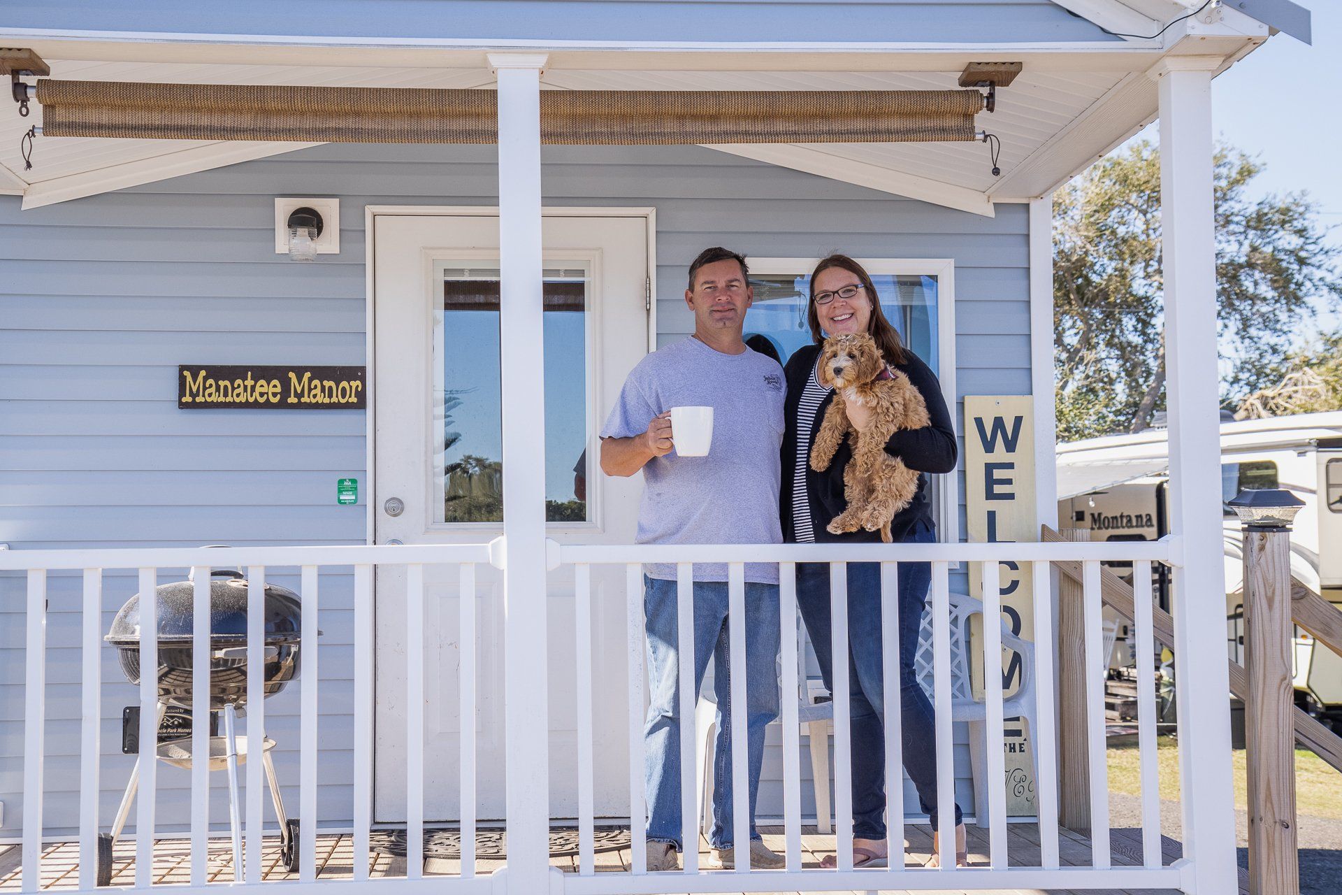 A man and a woman are standing on a porch holding a dog.