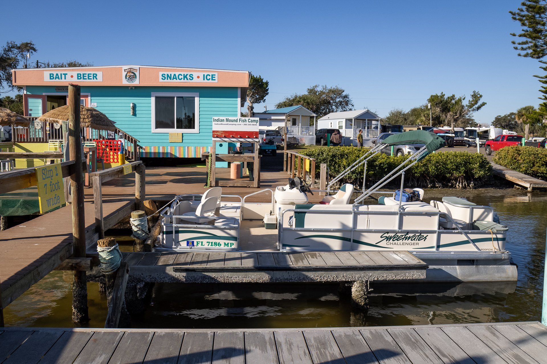 A pontoon boat is docked at a dock next to a building that says ice cream.