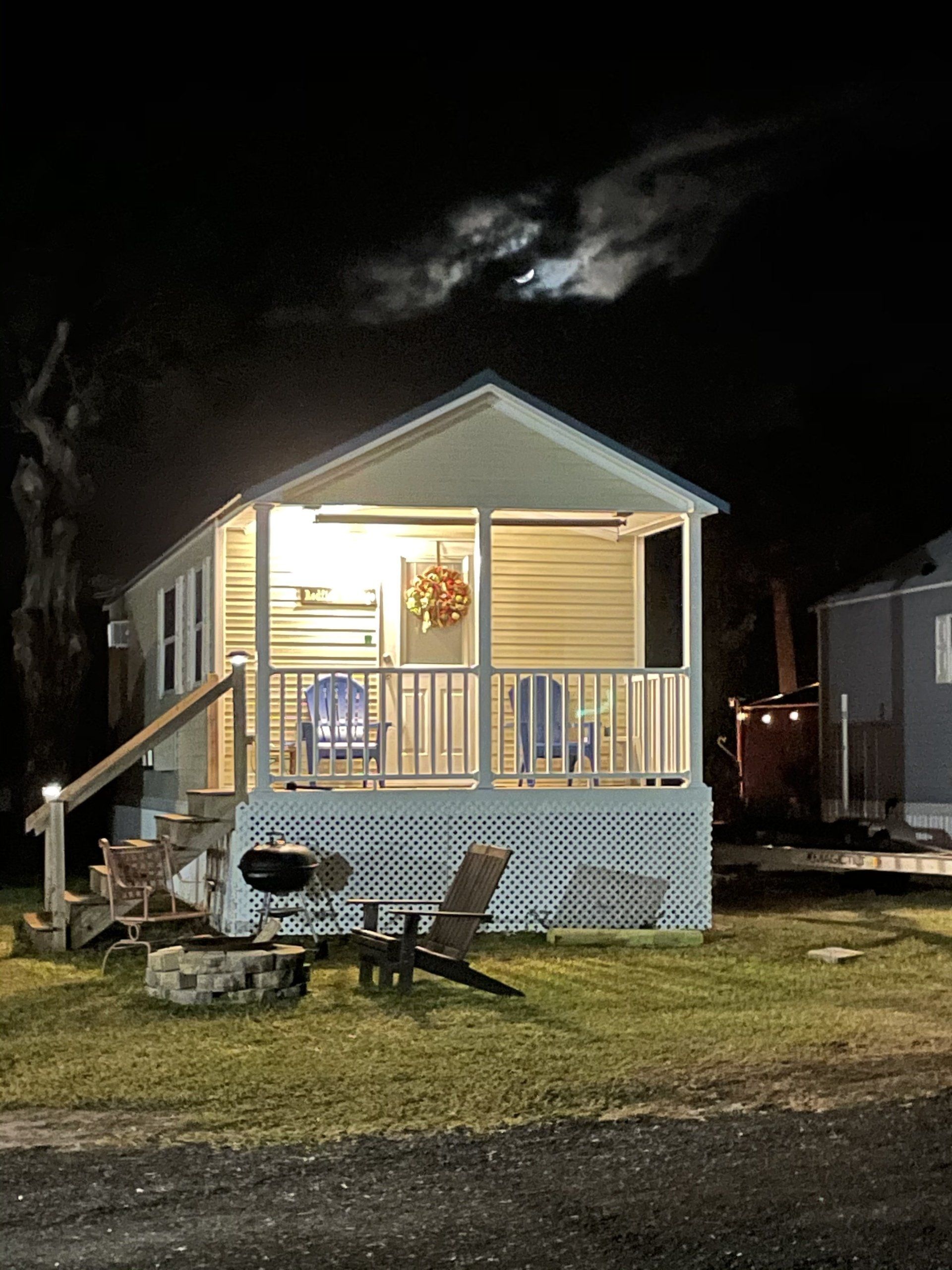 A mobile home is lit up at night with a fire pit in front of it.