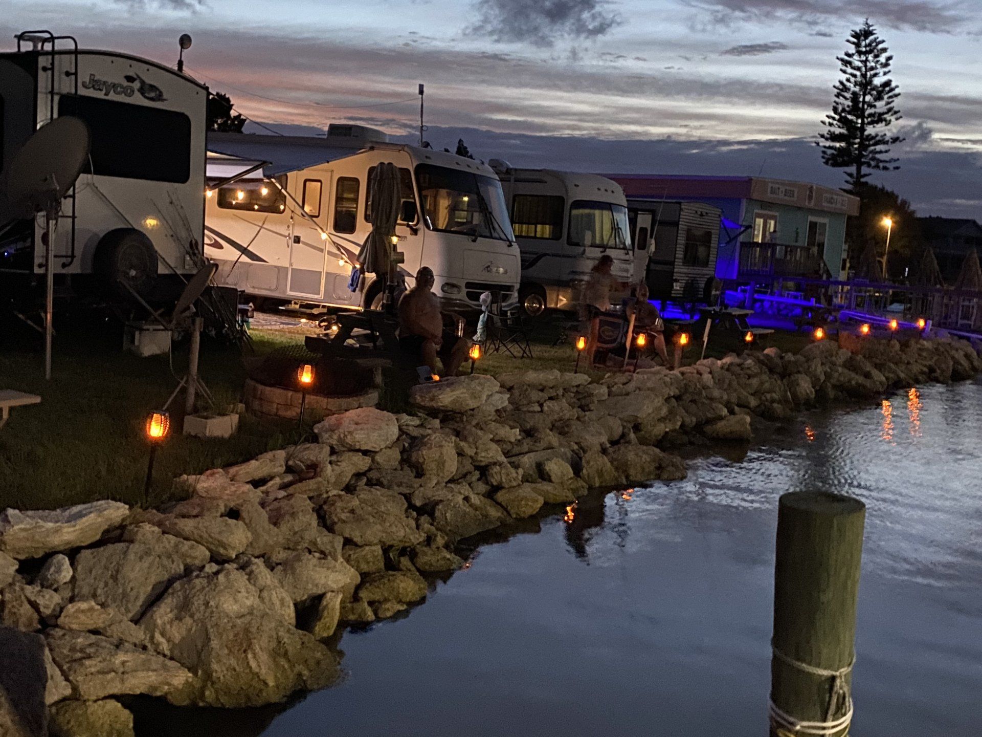 A row of rvs parked next to a body of water at night.