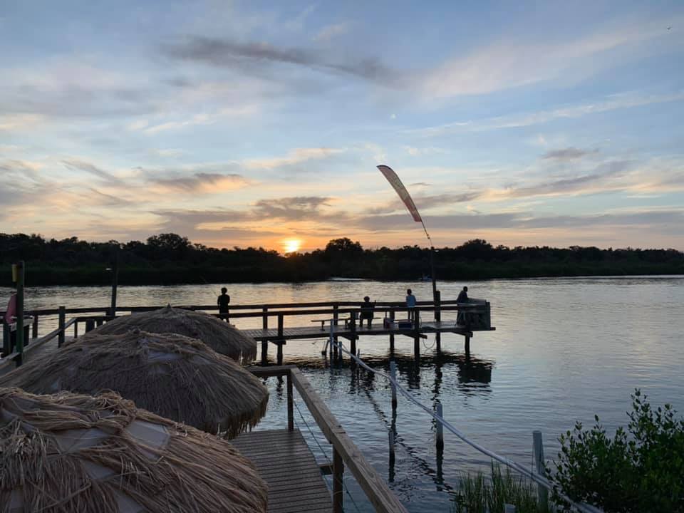 A group of people are standing on a dock overlooking a lake at sunset.