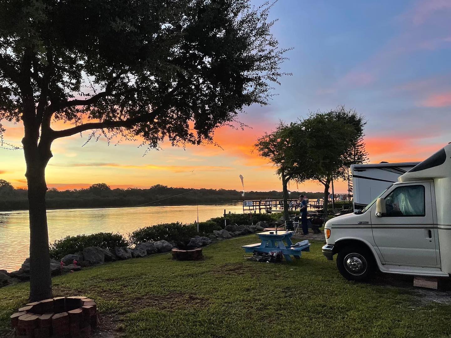 Rv parked in a grassy area next to a body of water at sunset.