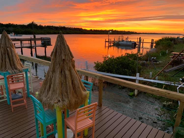 A deck with chairs and umbrellas overlooking a body of water at sunset.