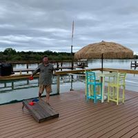 A man is standing on a dock next to a cornhole board.