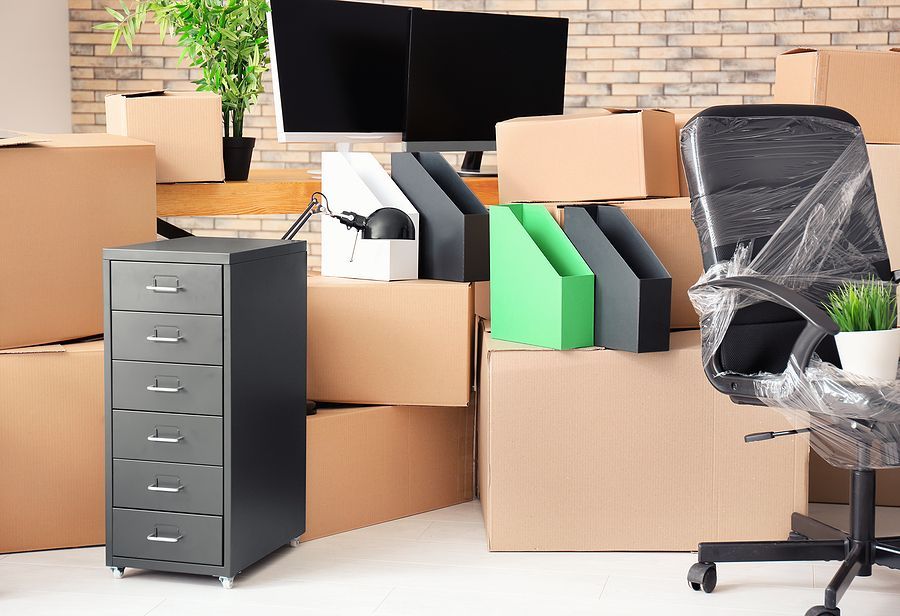 Stack of moving boxes, office chair, and equipment in an office.