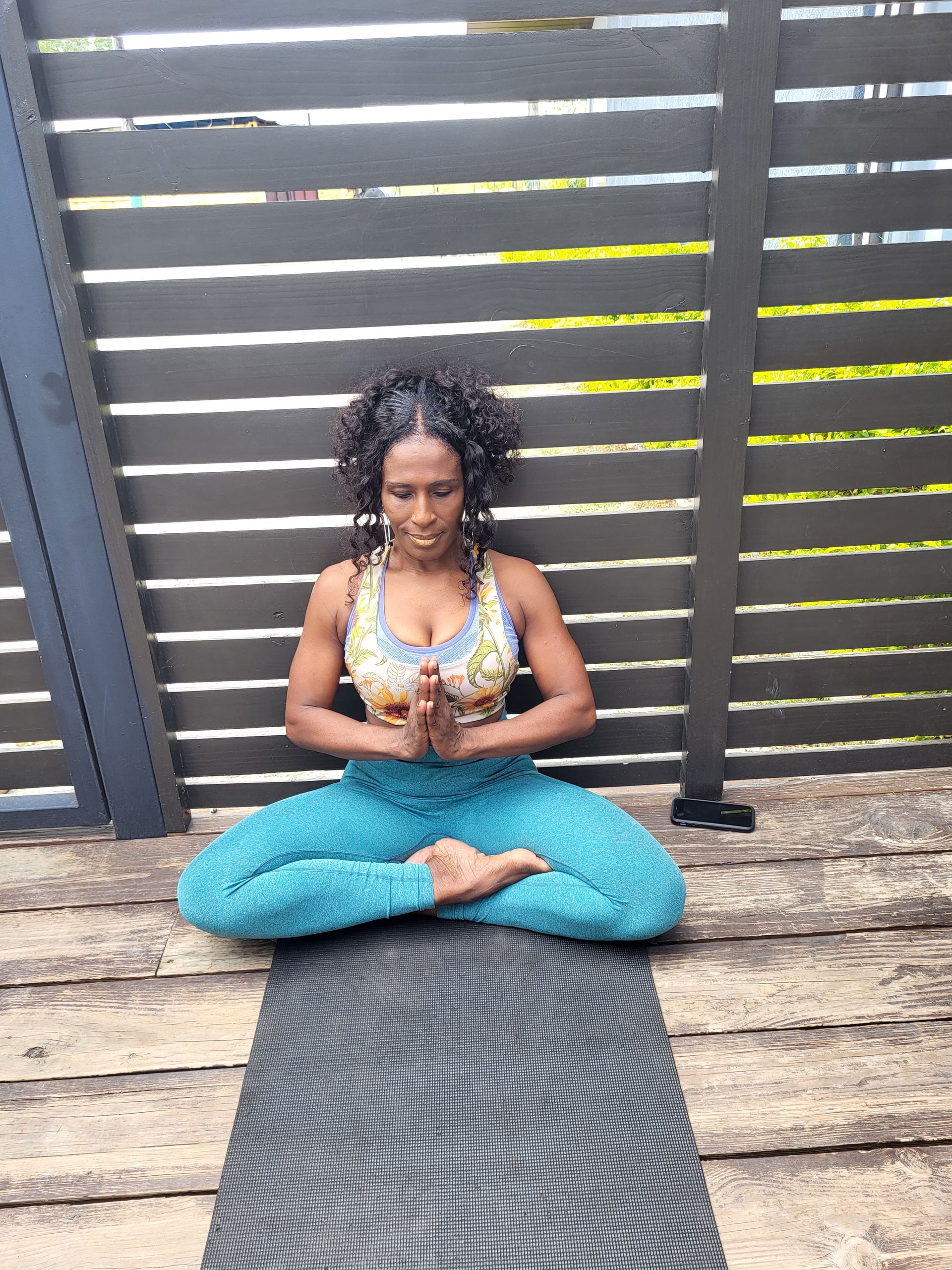 A woman is sitting on a yoga mat on a deck.