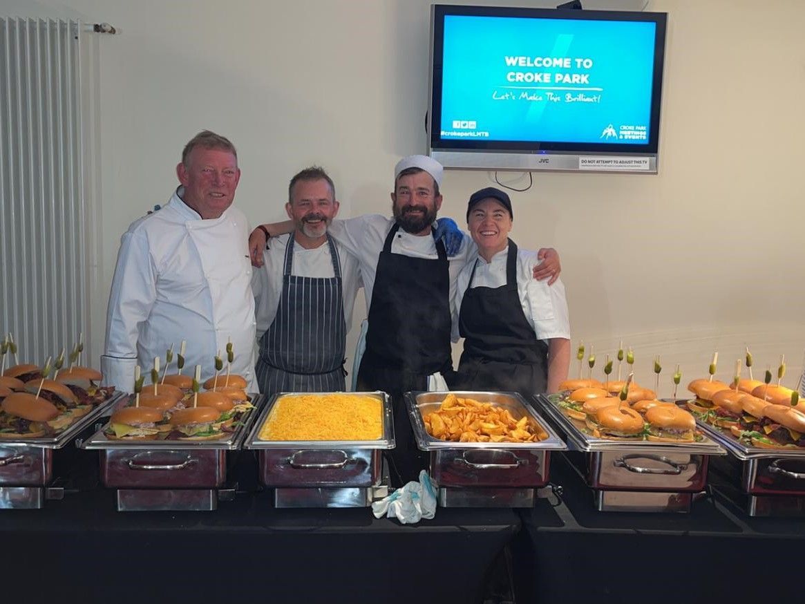 A group of chefs are posing for a picture in front of a buffet table filled with food.