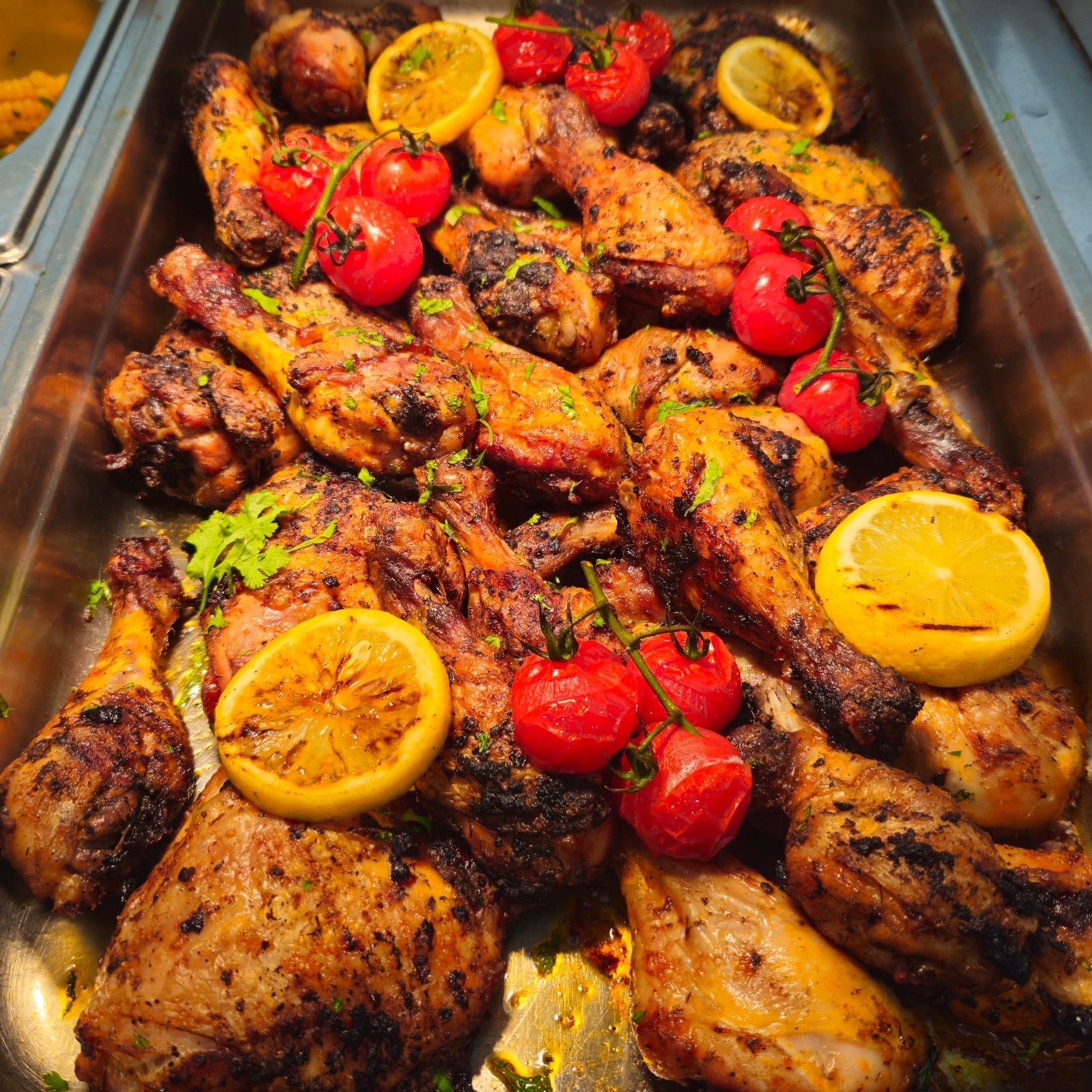 A tray of grilled chicken with lemon slices and tomatoes.