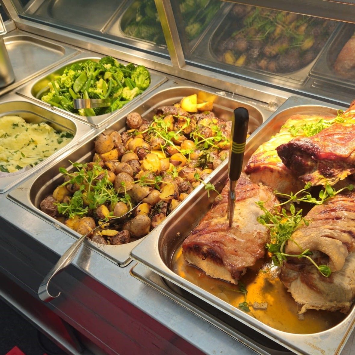 A buffet filled with meats and vegetables including broccoli and potatoes