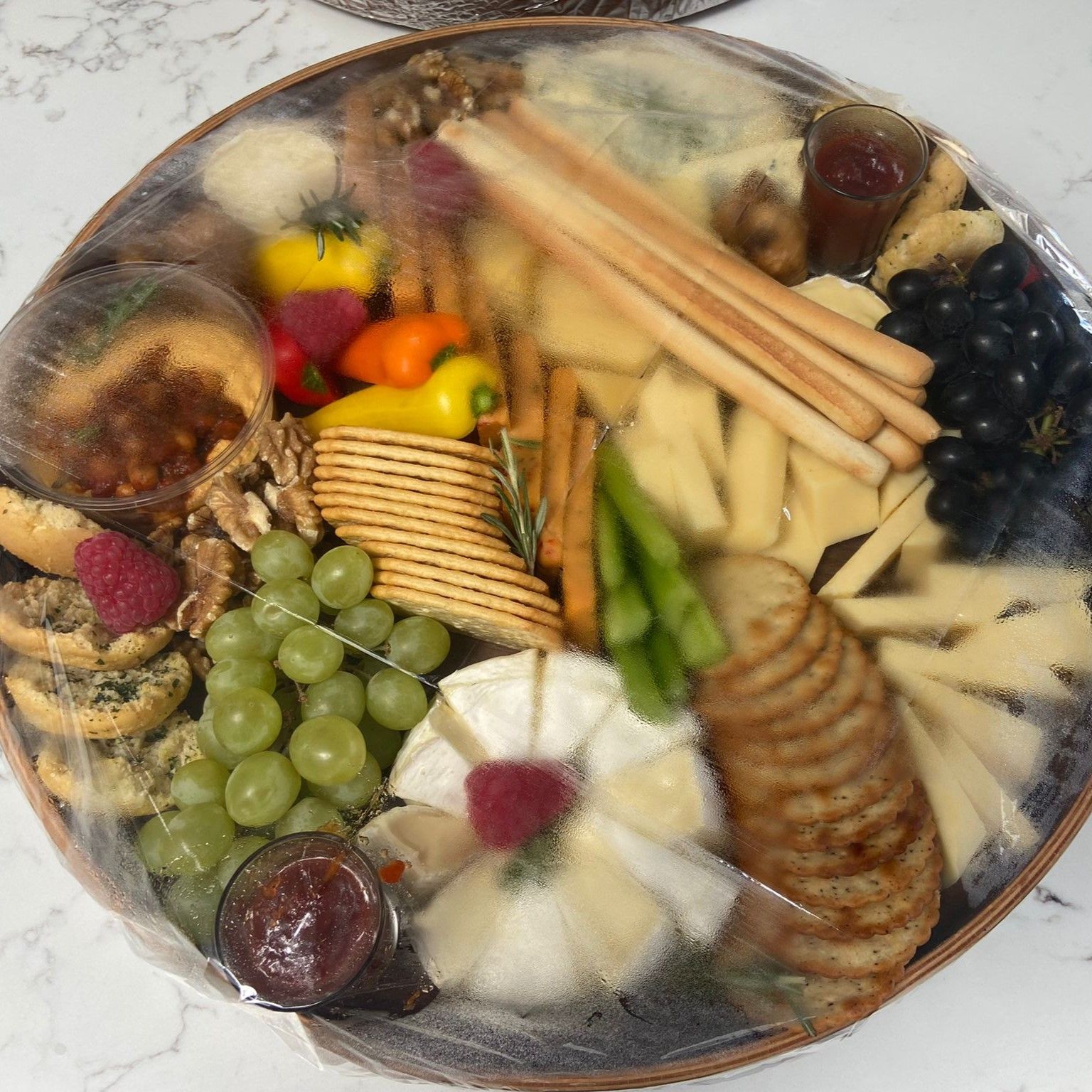 A tray filled with cheese , crackers , grapes and other food