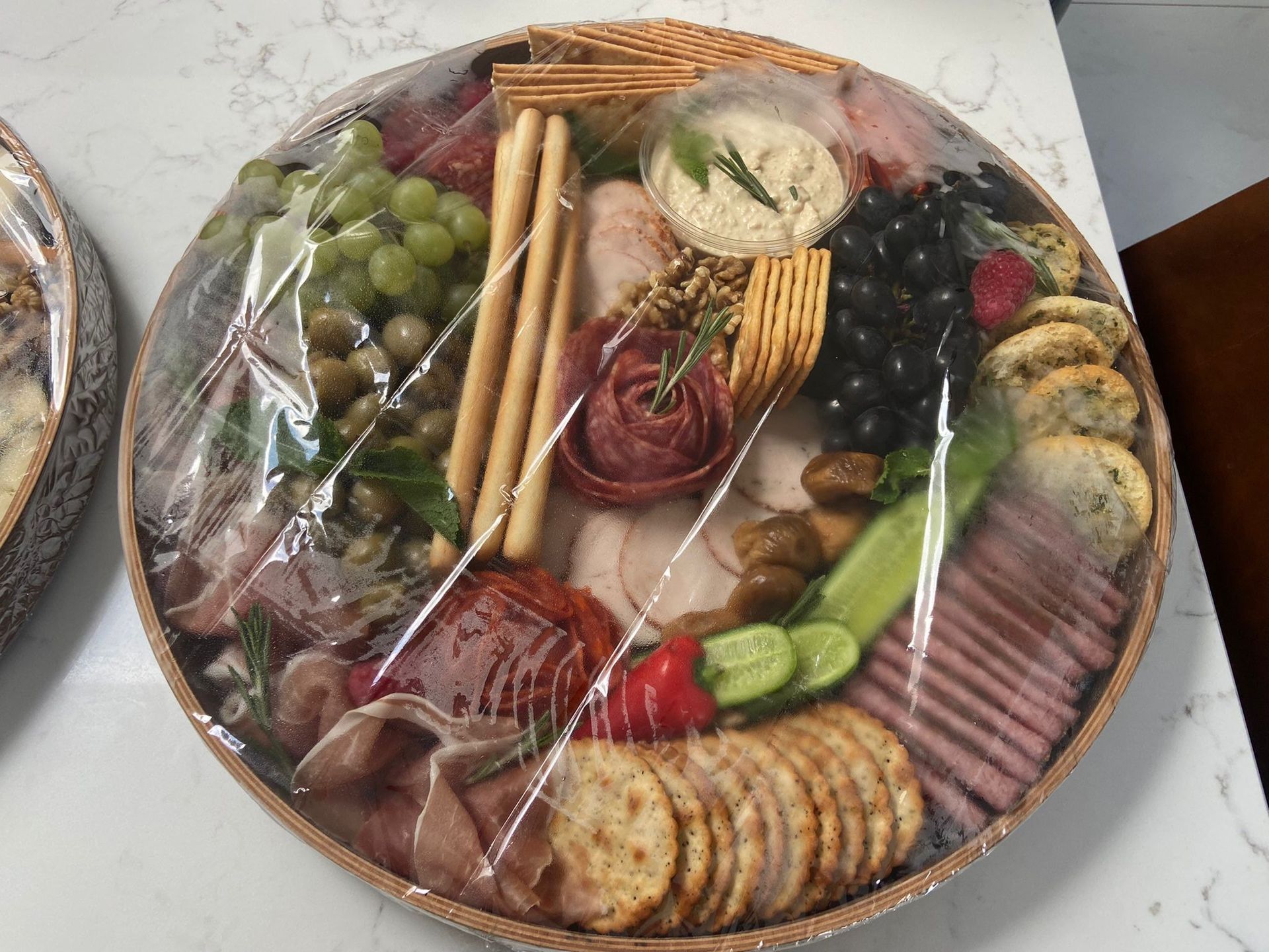 A large platter filled with meats , crackers , grapes , olives and vegetables.