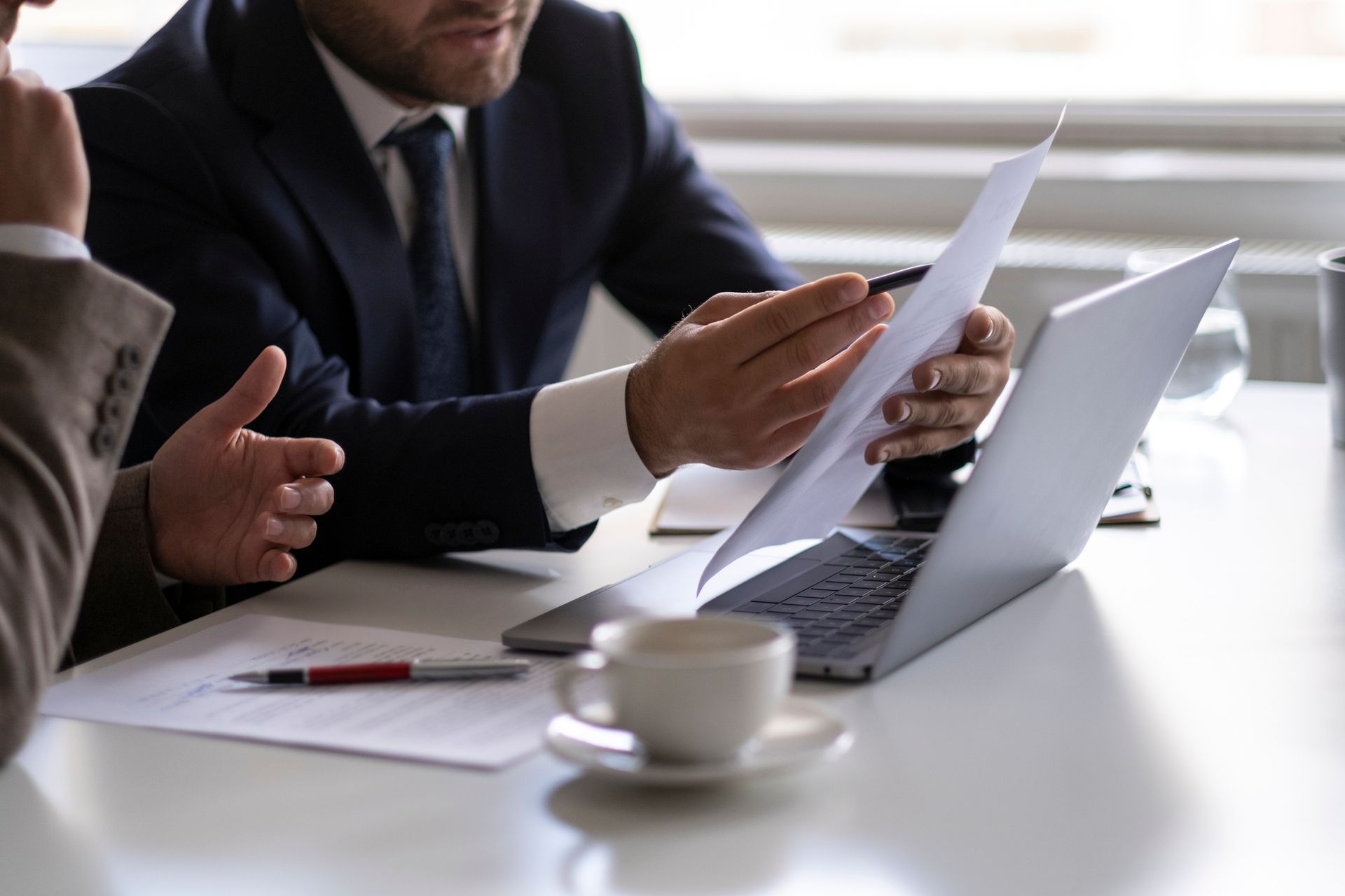 A man is holding a piece of paper in front of a laptop computer.