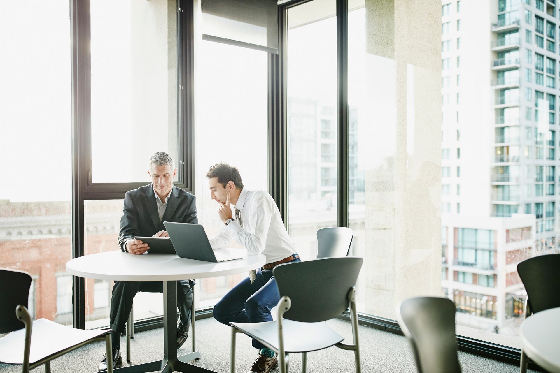 Two men are sitting at a table looking at a laptop.