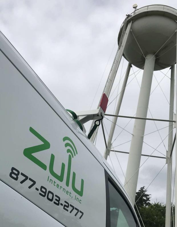 White van with Zulu Internet logo and phone number, water tower in background.