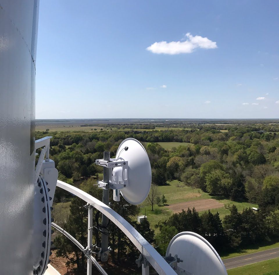 View from a communications tower.  Dish antennas overlook a green rural landscape under a blue sky.