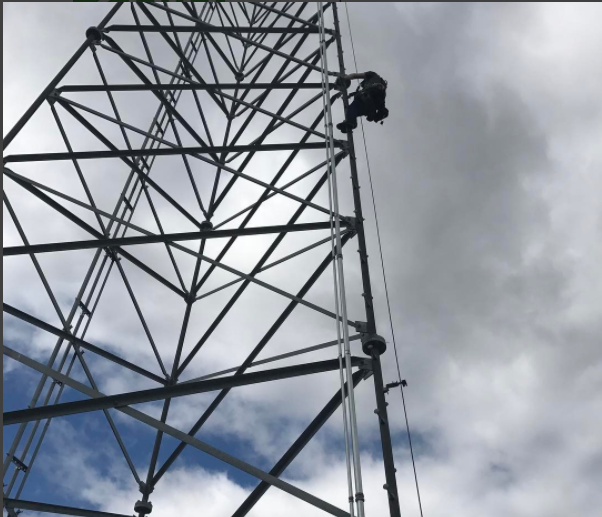 Person climbing a tall metal tower against a cloudy sky.