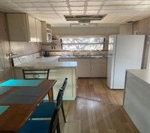 Kitchen With Wooden Floors, White Cabinets, a Refrigerator, and a Table With Chairs — Karumba Point Holiday Tourist Park in Karumba, QLD