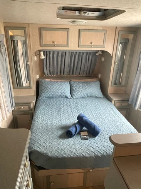 Bedroom in a Caravan With a Blue Bedspread and Rolled Towels — Karumba Point Holiday Tourist Park in Karumba, QLD