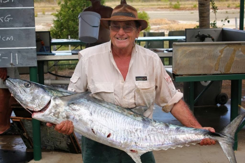 A man in a hat is holding a large fish in his hands.