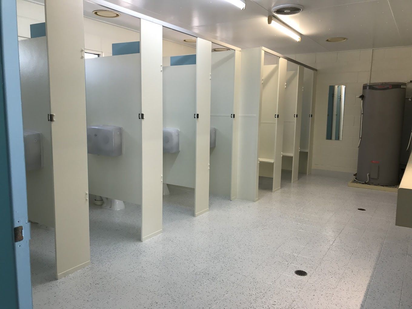 A bathroom with a lot of stalls and a mirror.