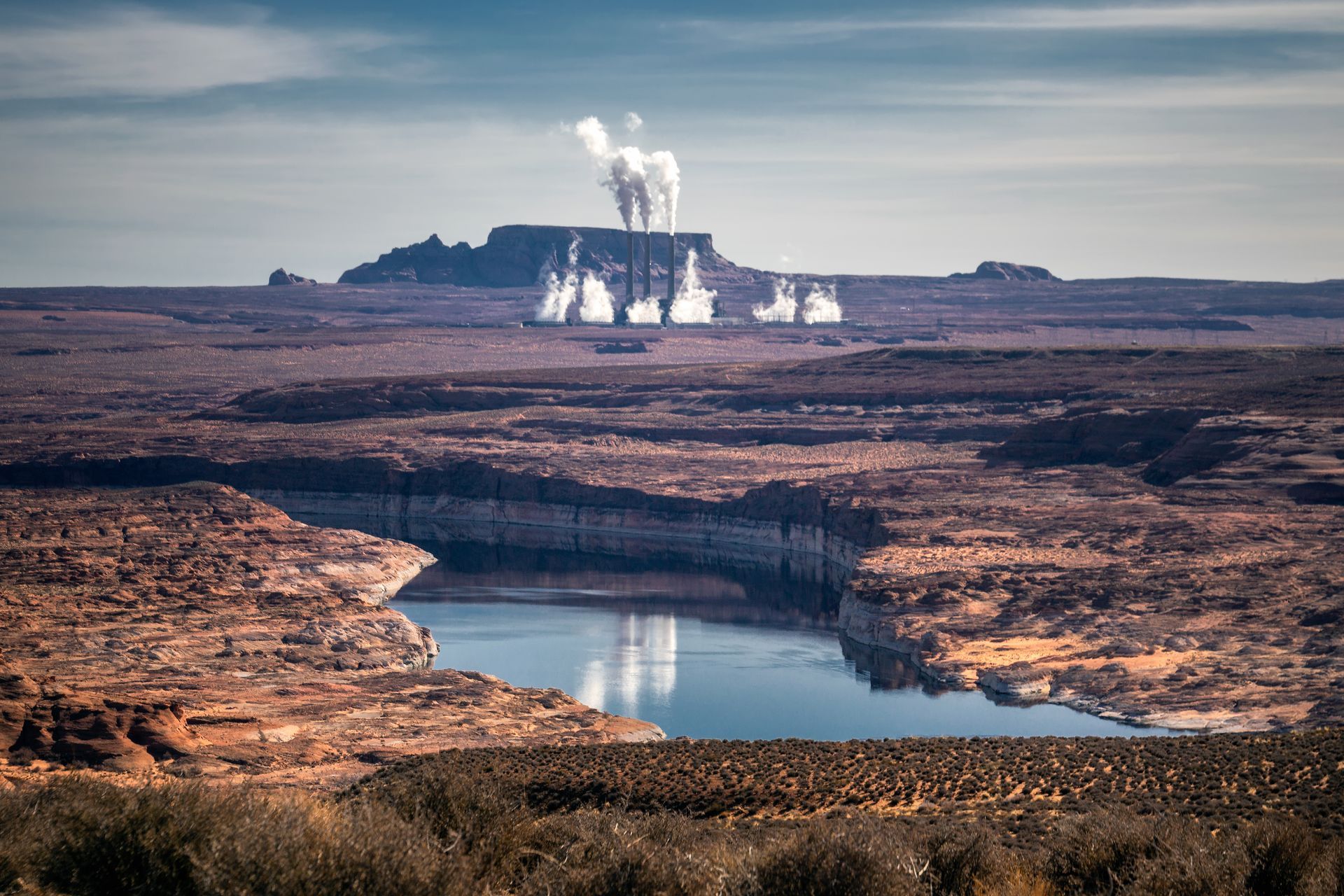 Una gran masa de agua en medio de un desierto con una central eléctrica al fondo.