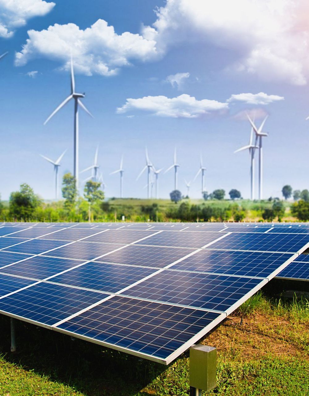 Un campo de paneles solares con turbinas eólicas al fondo.