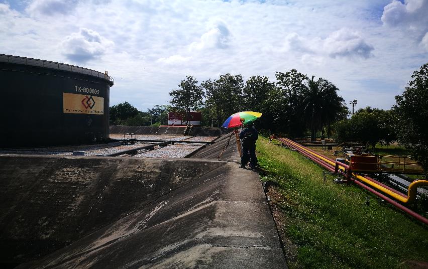 Un hombre que sostiene un paraguas camina por una acera al lado de un gran tanque.