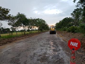 Una excavadora avanza por un camino de tierra al lado de un cartel rojo de prohibición.