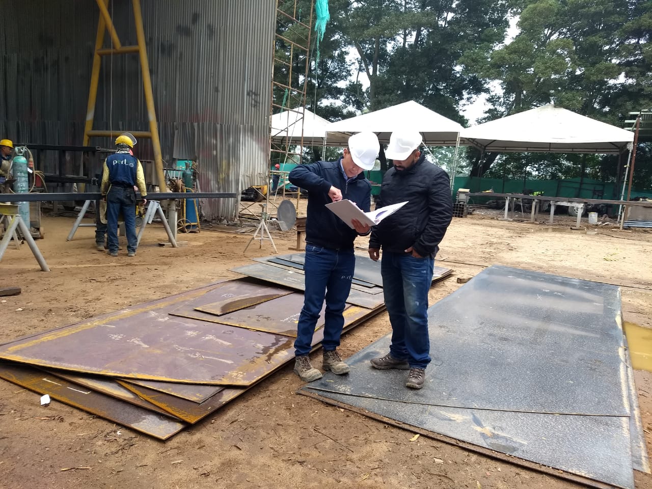 Dos hombres están parados uno al lado del otro mirando un trozo de papel.