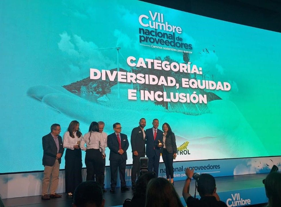 Un grupo de personas de pie frente a una pantalla grande que dice vii cumbre nacional de proveedores