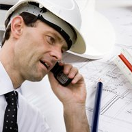 A man wearing a hard hat and tie is talking on a cell phone.