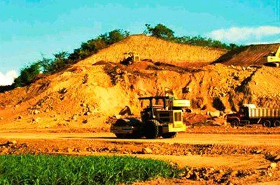 Una excavadora avanza por un camino de tierra al lado de una colina.