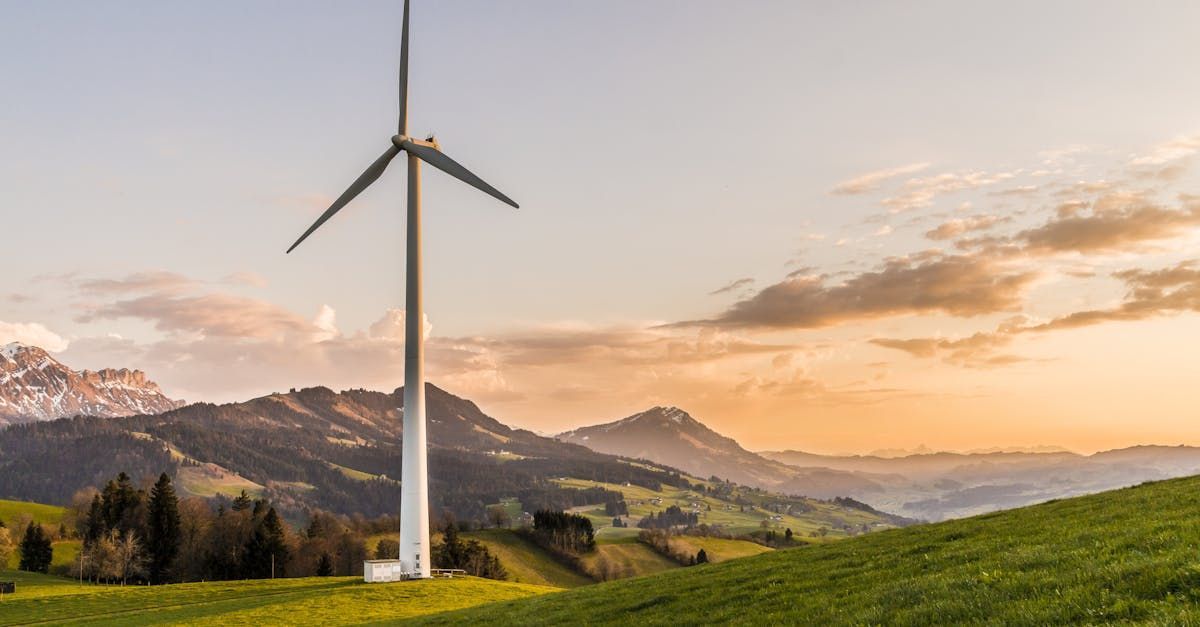 Una turbina eólica se encuentra en la cima de una colina cubierta de hierba con montañas al fondo.