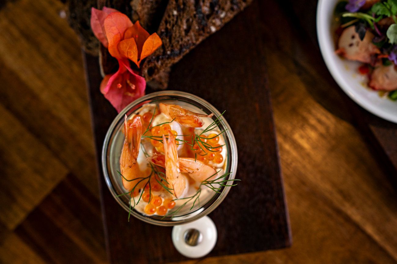 A bowl of shrimp is sitting on a wooden table next to a plate of food.