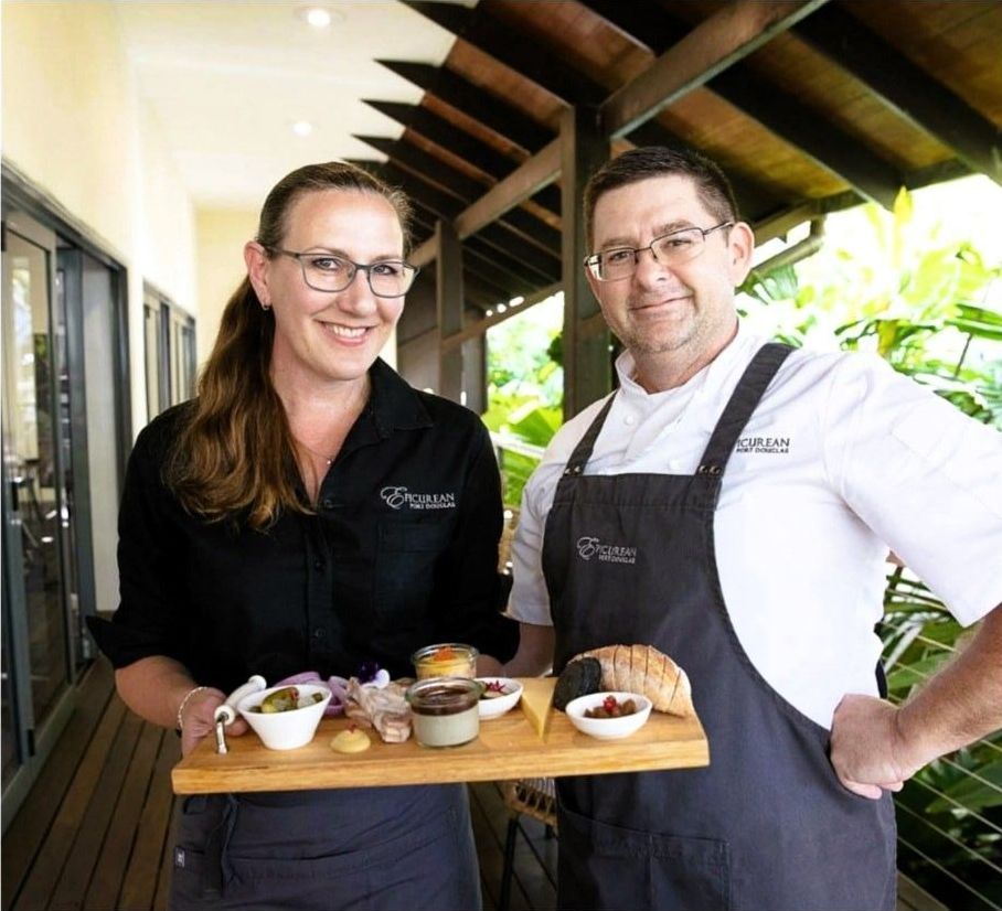 A man and a woman standing next to each other holding a tray of food