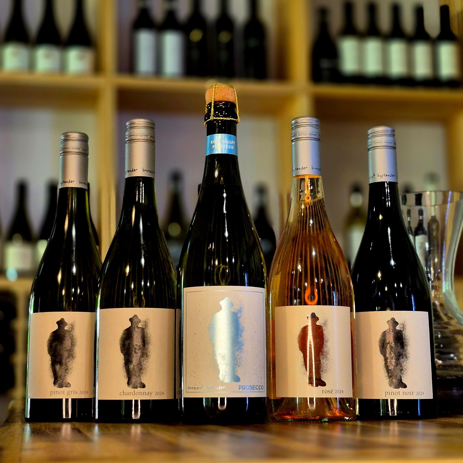 Five bottles of wine are lined up on a wooden table.