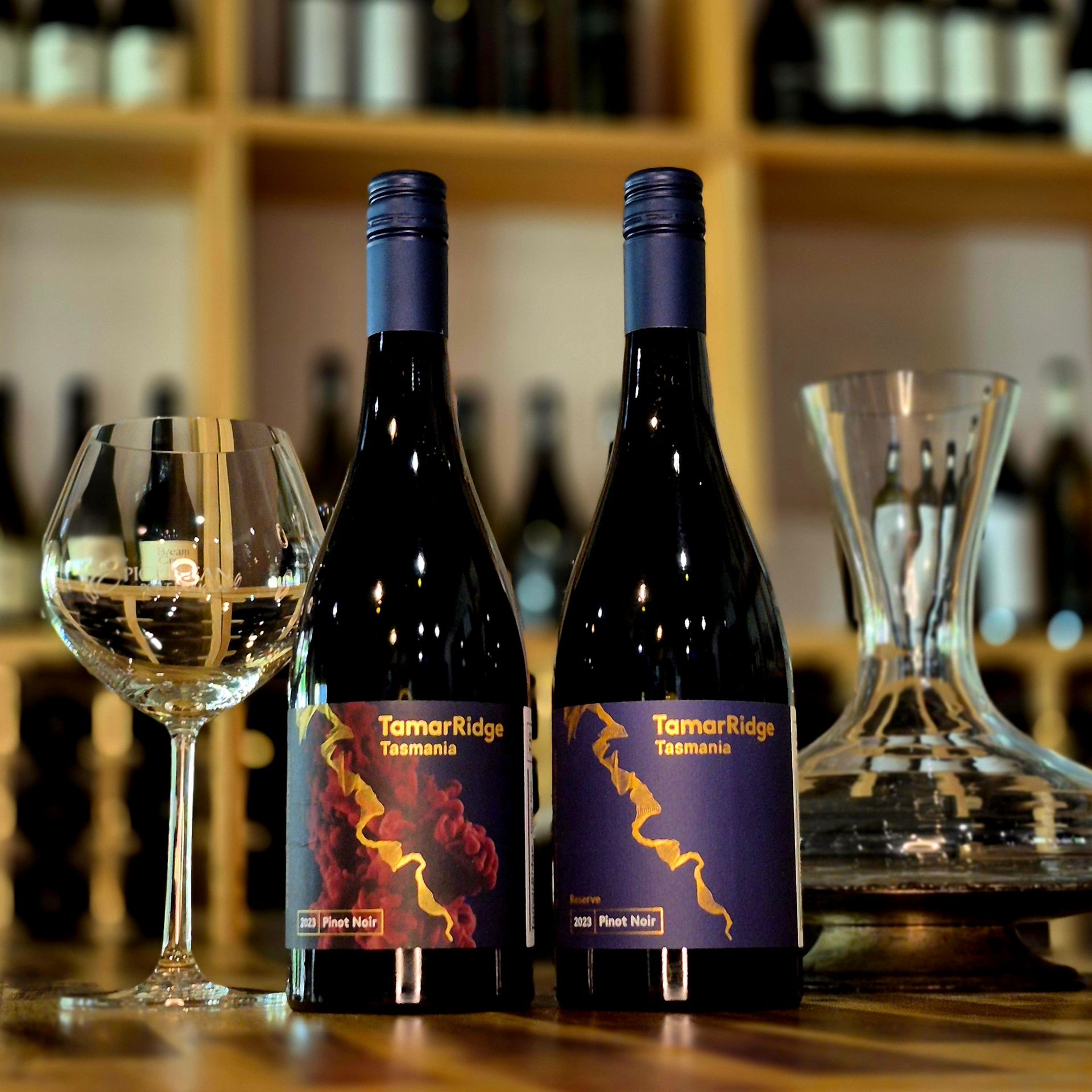 Two bottles of wine are sitting on a wooden table next to a wine glass.