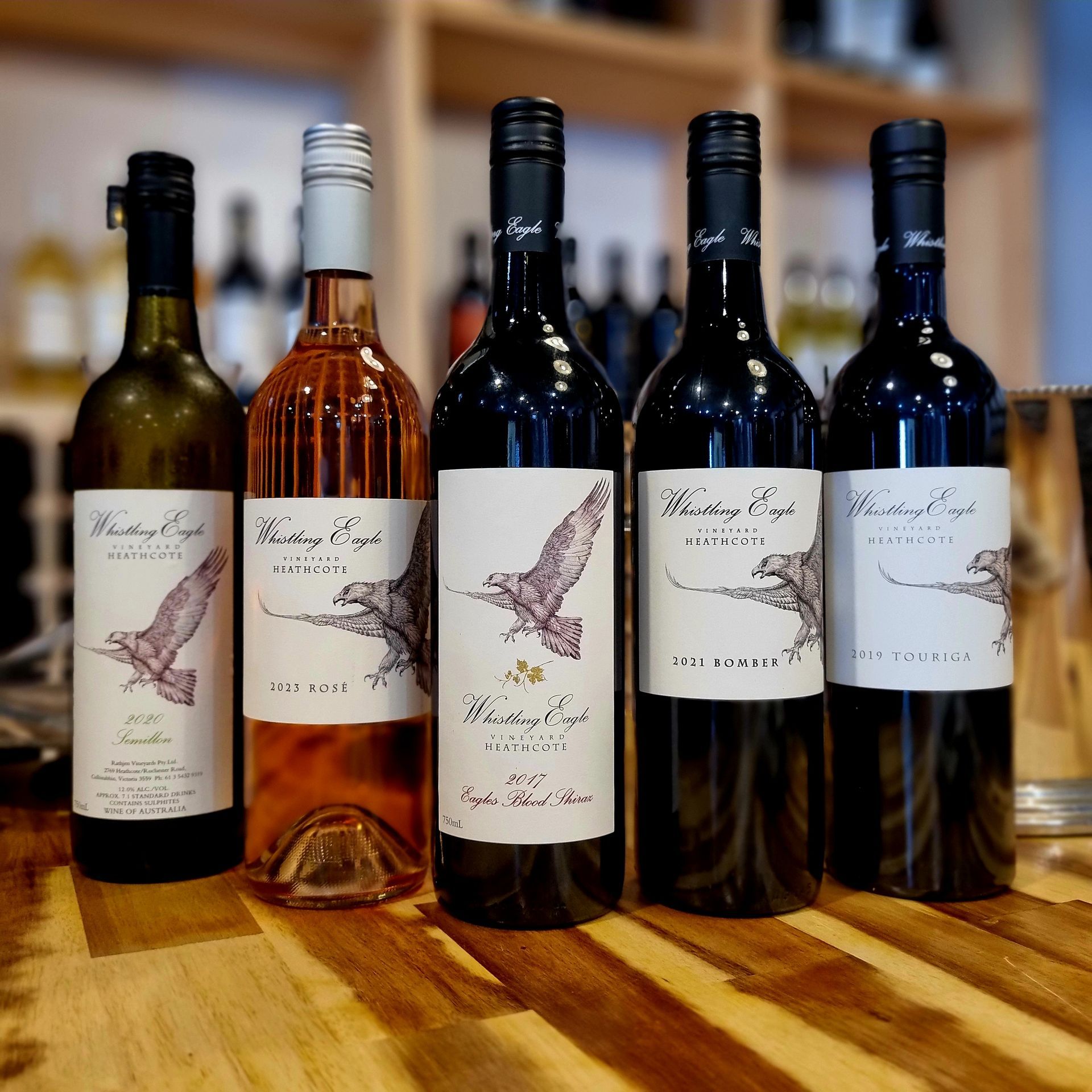 Five bottles of wine are lined up on a wooden table