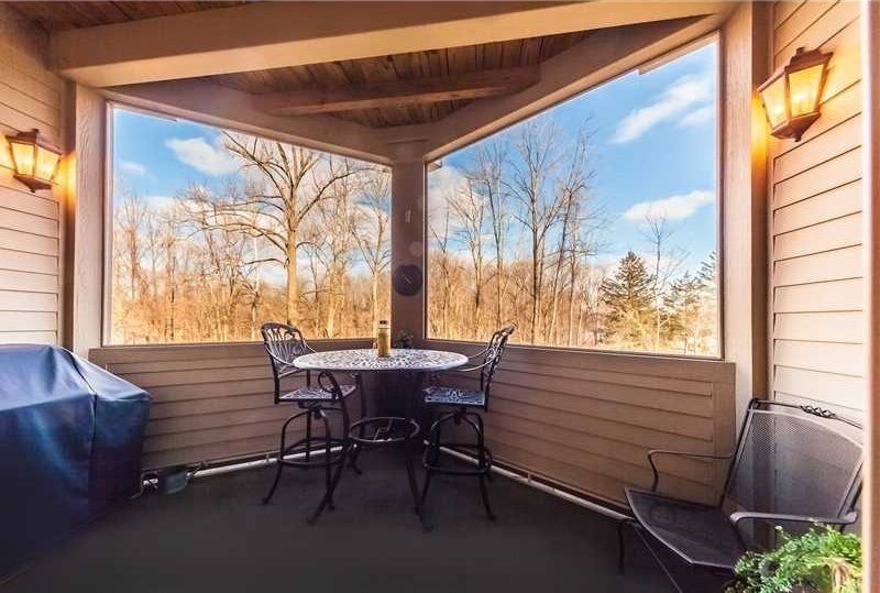 There is a table and chairs on the porch with a view of the woods.