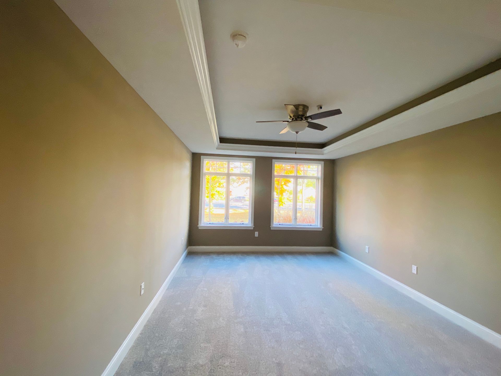 An empty room with a ceiling fan and two windows.