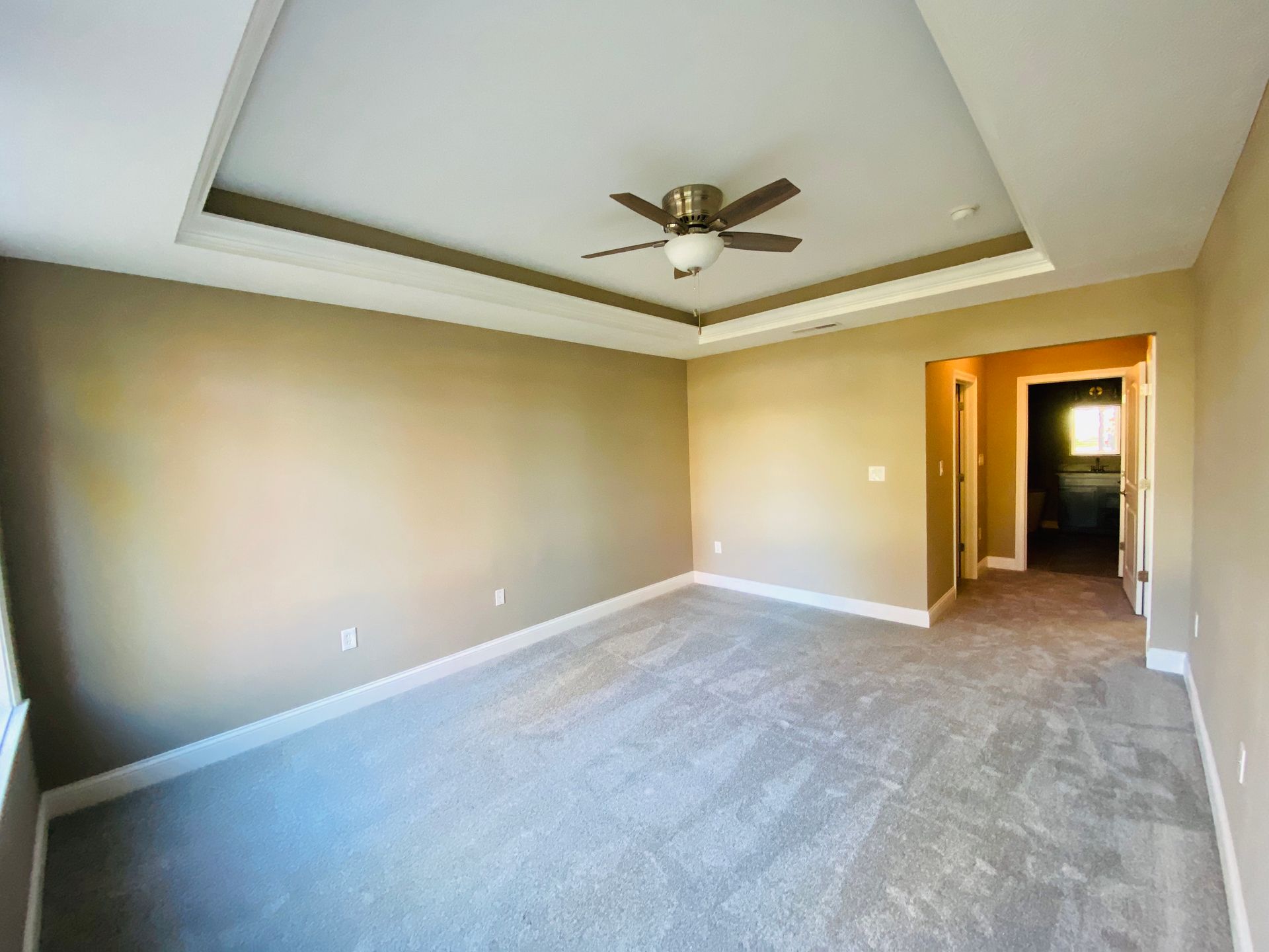 An empty bedroom with a ceiling fan and a carpeted floor.