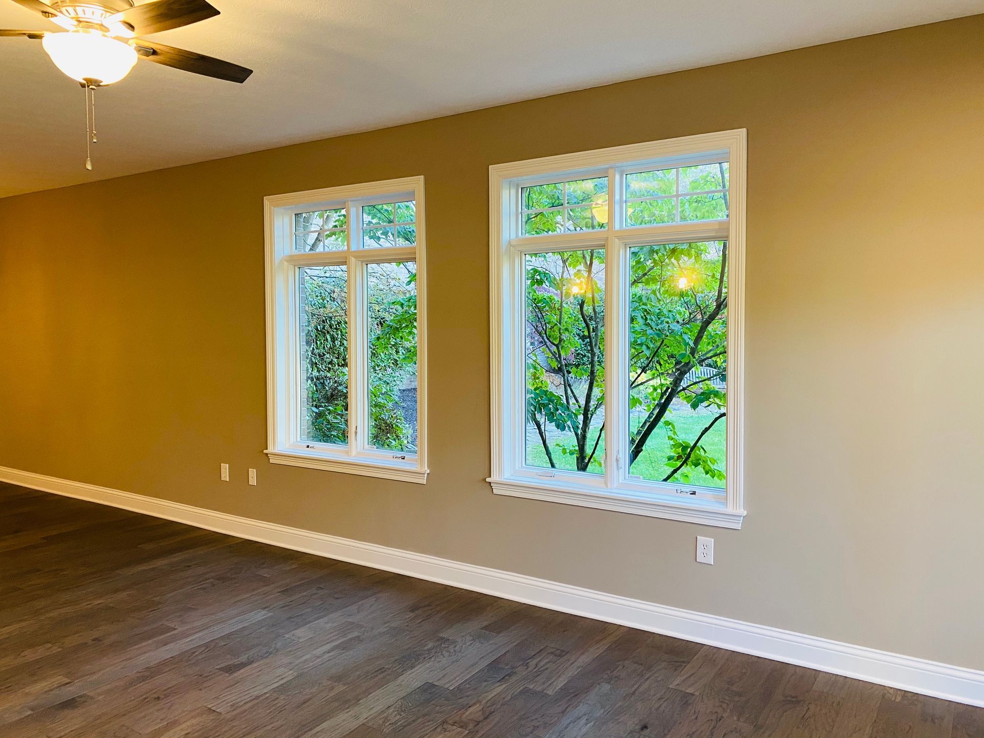 An empty living room with two windows and a ceiling fan.
